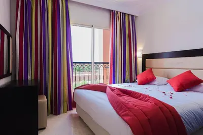 a bedroom with a bed with red pillows and a window at Palm Appart Hôtel Marrakech in Marrakech