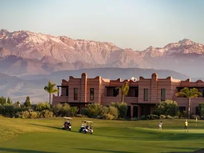 a building with golf carts on a green with mountains in the background at les jardins d'atlas waky palm golf in Marrakech