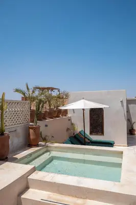 a swimming pool with an umbrella next to a house at Alrashid Marrakech Boutique Hotel & SPA in Marrakech