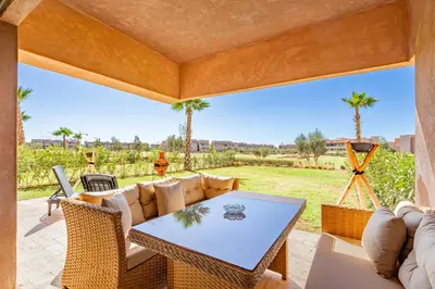 a patio with a table and chairs and palm trees at Résidence Golfique ,Piscine,Jardin terrasse privée in Marrakech