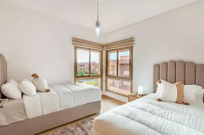 a white bedroom with two beds and a window at New! App Spacieux avec Piscine et Parking à Saphir in Marrakech