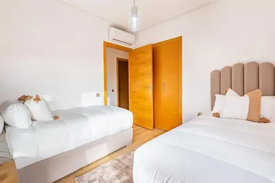 two beds in a bedroom with white walls and wooden floors at New! App Spacieux avec Piscine et Parking à Saphir in Marrakech