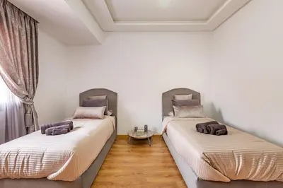 two beds in a room with white walls and wooden floors at New! App Émeraude Confort avec piscine & parking in Marrakech