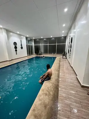 a man sitting on the edge of a swimming pool at Appartement 2 chambres Luxueuse centre Guéliz opr 15 in Marrakech