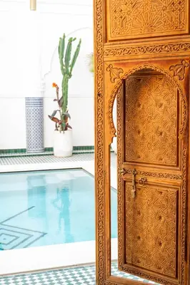 an ornate wooden door next to a pool at Riad Tamazigh in Marrakech