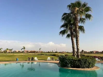 a palm tree sitting next to a swimming pool at Appartement Spacieux et Moderne avec une Vue sur Montagne et Piscine in Marrakech