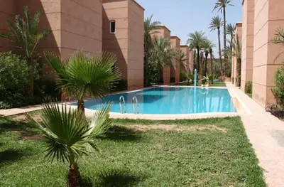 a swimming pool in front of a building with palm trees at Riad Camélia in Marrakech