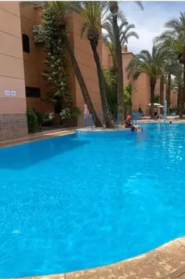 a large blue swimming pool with palm trees and a building at Riad Camélia in Marrakech