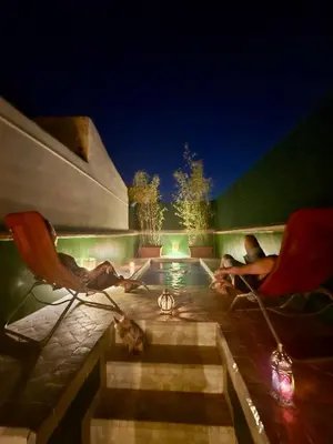 two people sitting in chairs by a pool at night at Riad Awatif le 36 in Marrakech