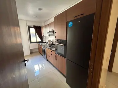 a kitchen with a black refrigerator and wooden cabinets at Burj Malak appartement dans une résidence privée avec piscine in Marrakech