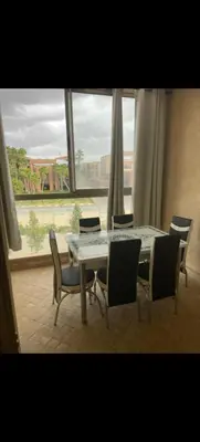 a dining room table and chairs with a large window at Appartement au coeur de Marrakech avec deux piscines et une charmante vue in Marrakech