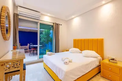a bedroom with a bed and a table and a window at Appartement avec terrasse et piscine in Marrakech