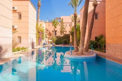 a swimming pool with palm trees and buildings at Riad Malika in Marrakech