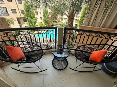 a balcony with two chairs and a table with orange pillows at Studio T2 vu sur piscine in Marrakech