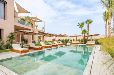 a pool with lounge chairs and umbrellas next to a building at Villa Piscine, Salle de Sport et Confort Moderne in Marrakech