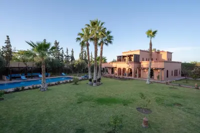 a large house with palm trees in a yard at Villa 5 suits with pool and montains view in Sraghna