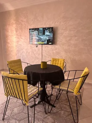 a dining room table with chairs and a tv on the wall at La rose à côté Carry in Marrakech