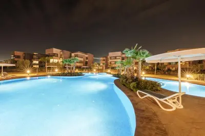 a swimming pool at night with a chair and an umbrella at Elegant Apartment in Prestigia Golf Marrakech in Marrakech