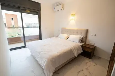 a bedroom with a white bed with a large window at Jawhar Appart A4 in Marrakech