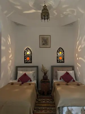 two beds in a room with a chandelier and two windows at Riad La Calèche in Marrakech