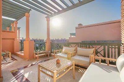 a patio with a couch and tables on a balcony at Appartement cosy Piscine et chill in Marrakech