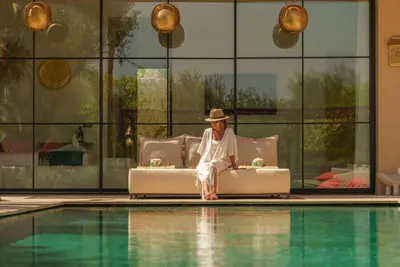 a man sitting on a couch next to a pool at Villa Eyline Amelkis Golf in Marrakech