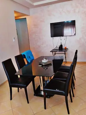 a dining room table with black chairs and a television at Appartement calme et spacieux in Marrakech