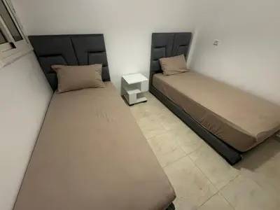 two beds in a small room with a night stand at Joli appartement nouveau Rez-de-chaussée in Marrakech