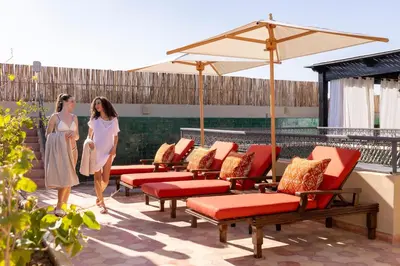 two women standing on a patio with chairs and an umbrella at Riad Laz Mouassine & Wellness in Marrakech