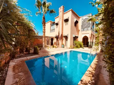 a swimming pool in front of a house with a palm tree at Naoura House in Marrakech