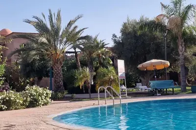 a swimming pool with an umbrella and palm trees at Dar Ou Bahssou in Marrakech