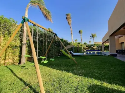 a swing set in a yard with a palm tree at Villa Léna détente en famille ! in Marrakech