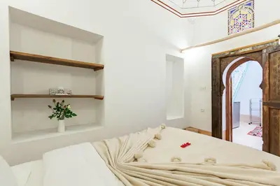 a white bedroom with a bed with a wooden headboard at Riad Petit Pouce 40m2 in der Medina mit Terrasse in Marrakech