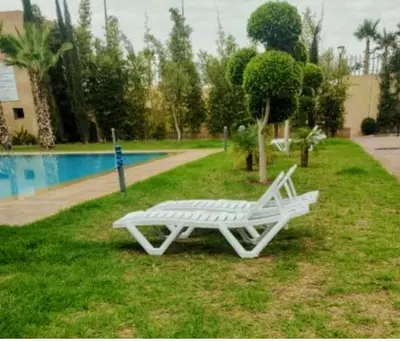 a white bench sitting in the grass near a pool at Appartement calme et élégant au coeur de Marrakech in Marrakech