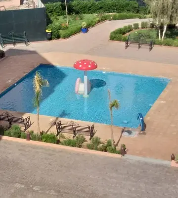 a swimming pool with a red umbrella next to benches at Somptueux appartement avec terrasse et piscines in Marrakech