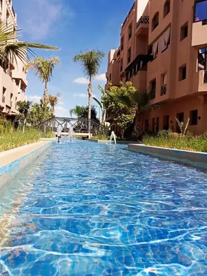 a swimming pool in a resort with palm trees and buildings at Somptueux appartement avec terrasse et piscines in Marrakech