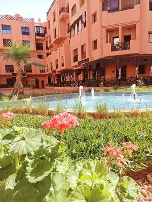 a garden in front of a building with people playing in a swimming pool at Somptueux appartement avec terrasse et piscines in Marrakech