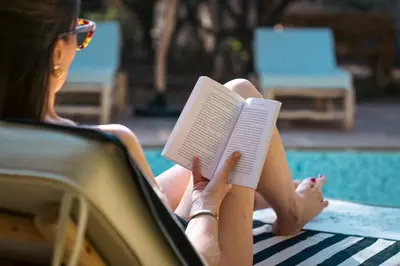 a woman sitting in a chair reading a book by a pool at La Villa Safran Ailleurs sous les Oliviers in Marrakech
