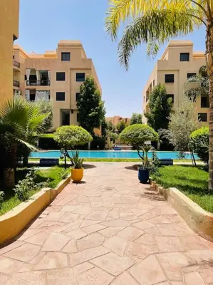 a walkway in a courtyard with palm trees and buildings at Confort et Style Studio Chic avec Piscine in Marrakech