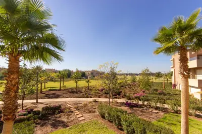 a garden with palm trees and a building at Relaxation et Confort a Prestigia -10 min du centre in Marrakech