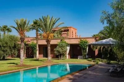 a swimming pool in front of a house with palm trees at Exceptional villa on 10,000 meter square with heated pool in Marrakech