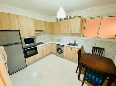a kitchen with wooden cabinets and a table and a refrigerator at Appart Moderne Calme & Climatisé in Marrakech