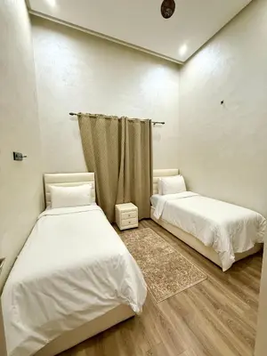 two beds in a room with white walls and wooden floors at Appartement sympathique in Marrakech