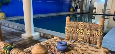 a rattan couch sitting next to a swimming pool at Apart Hotel Larabi in Marrakech