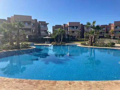 a large blue swimming pool with buildings in the background at Appartement de vacances à Prestigia golf city rez jardin in Marrakech