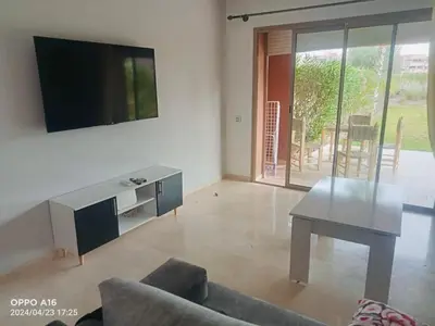 a living room with a table and a tv on a wall at Appartement de vacances à Prestigia golf city rez jardin in Marrakech