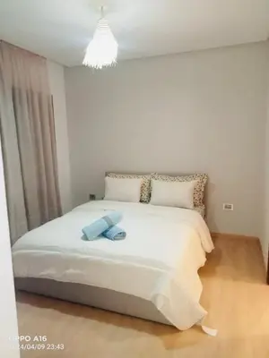 a bedroom with a large white bed with a chandelier at Appartement de vacances à Prestigia golf city rez jardin in Marrakech