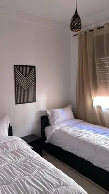 two beds in a room with white sheets and a window at Familial Cosy Appart in Marrakech