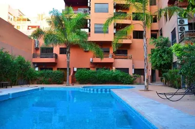a swimming pool in front of a building with palm trees at Apartment in Centre of Marrakech in Marrakech