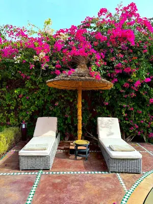 two chairs and a table with a umbrella and pink flowers at Palais Mars in Marrakech